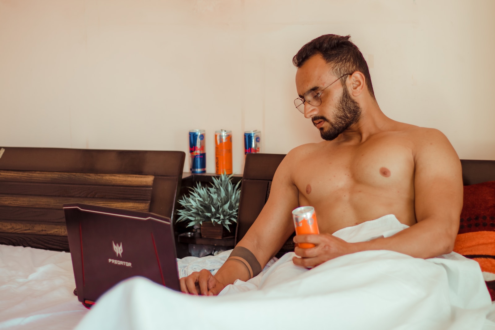 topless man holding orange plastic bottle sitting on bed